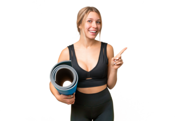 Blonde sport woman going to yoga classes while holding a mat over isolated chroma key background pointing to the side to present a product