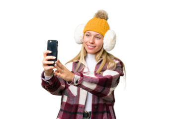 Young pretty blonde woman wearing winter muffs over isolated chroma key background making a selfie