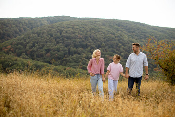 Family enjoys a leisurely walk in a sunlit meadow surrounded by lush green hills during a pleasant...