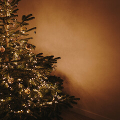 Christmas tree decorated with toys and warm garland lights on tan brown wall. Aesthetic Christmas,...