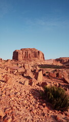 Fototapeta premium A stunning desert scene unfolds with unique rock structures and textured ground, surrounded by sparse vegetation. Under the bright blue sky, this space evokes serenity and raw beauty.