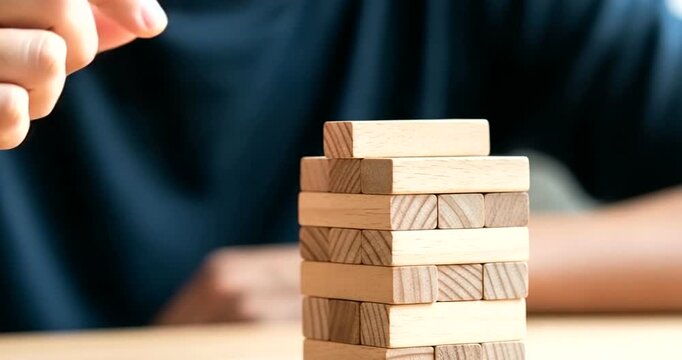 Closeup of a persons hand carefully placing a wooden block on a tower