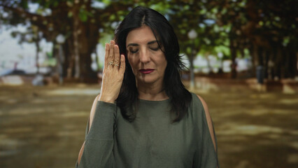 Woman presses ringed hand against face in forest clearing amidst green branches; quiet reflection solitude.