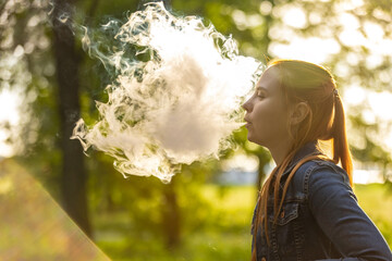 An young woman with long, red hair vaping in a forested area. The person is captured from the side,...