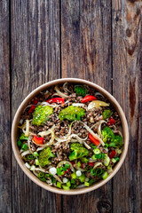 Lunch in disposable box. Takeaway Chow Mein noodles with ground beef, broccoli and red bell pepper on wooden table. Top view