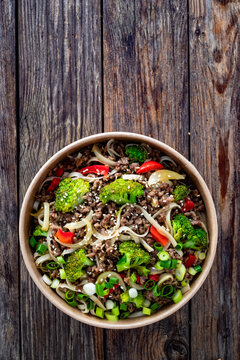 Lunch in disposable box. Takeaway Chow Mein noodles with ground beef, broccoli and red bell pepper on wooden table. Top view