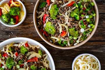 Lunch in disposable box. Takeaway Chow Mein noodles with ground beef, broccoli and red bell pepper on wooden table. Top view

