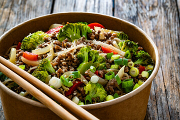 Lunch in disposable box. Takeaway Chow Mein noodles with ground beef, broccoli and red bell pepper on wooden table	

