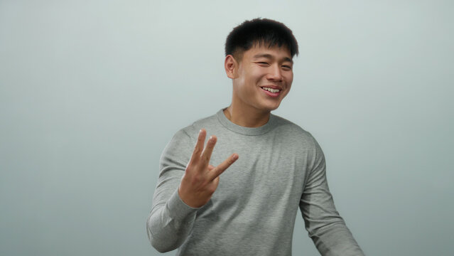 Young chinese man in grey sweater over isolated white background expressing gestures with hands, smiling with positivity.