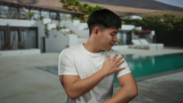 Young chinese man enjoying outdoor pool at a luxurious resort hotel, displaying a cheerful demeanor and casual style.