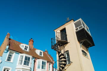 Abstract view of a narrow but tall seaside lookout tower on the Suffolk, UK coast. Nearby are large promenade houses used as summer holiday lets.