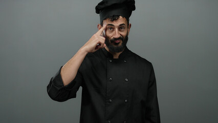 Hispanic male chef in black uniform gestures thoughtfully against grey backdrop, suggesting...