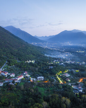 Aerial view of the tranquil town nestled amidst rolling hills, where warm lights flicker against the cool twilight, Santo Stefano del Sole, Irpinia, Campania, Italy.