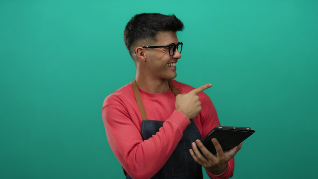 Young man with glasses and apron holding tablet against green background, appearing thoughtful and engaged. - Powered by Adobe