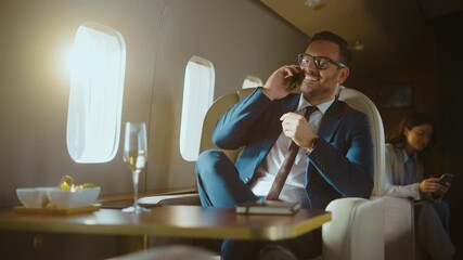 Confident and successful businessman talking on his smartphone while traveling in a luxurious private jet, enjoying a first-class flight and closing deals while flying to his destination - Powered by Adobe
