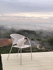 A white cat with black stripes on its face sits on a chair, looking at the morning mist from a high angle.