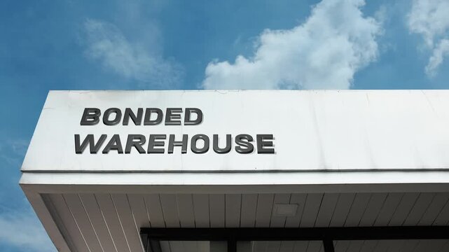 Bonded Warehouse word sign clearly displayed on the industrial facade of a secured storage facility beneath a crisp blue sky, signifying customs control, deferred duties, and international logistics