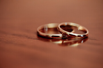 Two gold wedding rings sit on a warm wooden surface, symbolizing love and commitment. Soft focus...