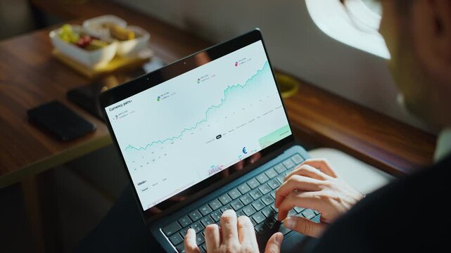 Professional financial analyst working on a laptop, checking stock market currency charts and data while traveling in a first-class cabin on a commercial airplane or a private jet