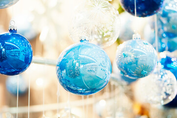 Blue glass Christmas ornaments hang in a festive store display, their shiny surfaces reflecting lights and surroundings. Ideal for holiday decor, winter celebrations, and retail promotions.