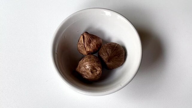 Fermented black solo garlic or monobulb garlic in a white bowl. It has the flavour of the garlic clove but is somewhat milder and lightly perfumed.