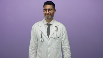 Man in white lab coat wearing stethoscope and visible face posed against purple studio wall; compassion trust professional healthcare.