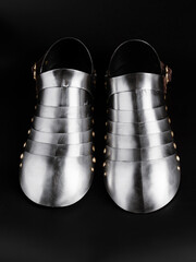 Close-up view of a pair of polished medieval steel sabatons laying on a black surface. Design displays historical craftsmanship. Iconic representation of armored footwear from the Middle Ages.