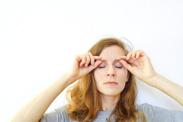Redhead female practicing brow bone massage with gentle finger pressure. Concepts of facial circulation boost, wrinkle prevention routine, holistic skincare trend, and tension release exercise.