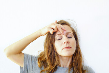 A woman aged 30+ works on the frown lines between her eyebrows using self-massage with her fingers. Symbolizes alternative medicine practice, mindful beauty rituals, and natural rejuvenation trend.