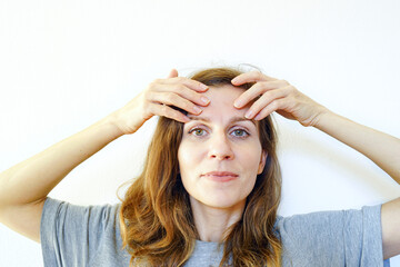 A woman massages her forehead, smoothing the skin along the massage lines with her fingers. Symbolizes aging prevention practice, non-invasive facial care, slow beauty ritual, and mindful rejuvenation