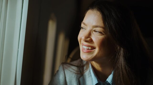 Happy successful businesswoman enjoying the warm sunlight on her face while looking out the window during a train journey. A beautiful female passenger is smiling feeling optimistic about her trip