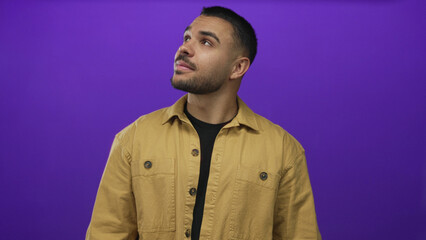 Man face looking up in purple studio setting wearing brown jacket with slight head tilt and casual pose; curiosity.