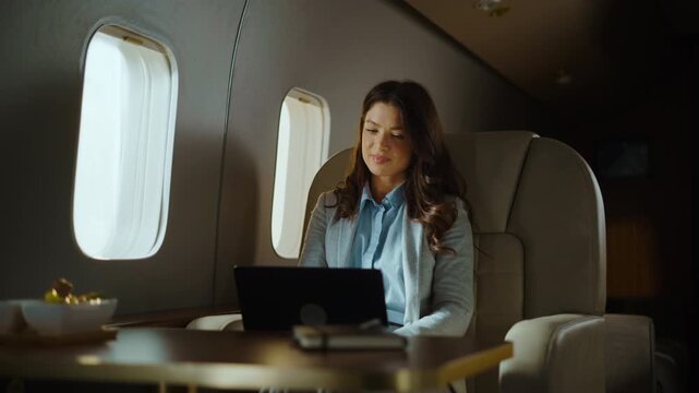 Confident businesswoman flying on a private jet and working on her laptop computer. A wealthy female entrepreneur sitting in a luxury first-class airplane cabin during a business trip