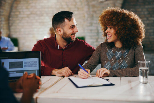 Smiling couple look happily at each other while signing a financial document in a consultation meeting with an advisor. - Powered by Adobe