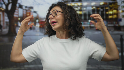 Middle aged hispanic woman shows talking gesture with hands on a busy city street; communication expression engagement conversation.