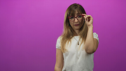 Woman adjusts red cat eye glasses with right hand in studio against a magenta wall; thoughtful curiosity.