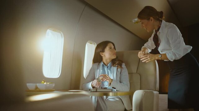 Elegant businesswoman enjoying a glass of champagne and having a pleasant conversation with a flight attendant during a comfortable journey on a luxurious private jet in first class