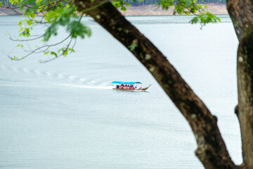 A long-tail boat carrying tourists with a blue canopy glides across a peaceful lake in Thailand, surrounded by calm water and natural scenery. Perfect image for travel and tourism concepts.