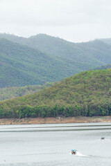 A long-tail boat carrying tourists with a blue canopy glides across a peaceful lake in Thailand, surrounded by calm water and natural scenery. Perfect image for travel and tourism concepts.