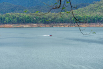 A long-tail boat carrying tourists with a blue canopy glides across a peaceful lake in Thailand, surrounded by calm water and natural scenery. Perfect image for travel and tourism concepts.