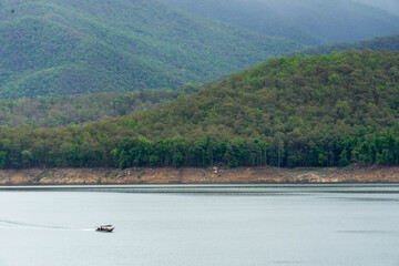 A long-tail boat carrying tourists with a blue canopy glides across a peaceful lake in Thailand, surrounded by calm water and natural scenery. Perfect image for travel and tourism concepts.