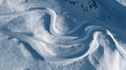 Aerial view of curved ski tracks in deep freeride snow with mountain terrain patterns