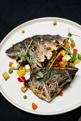 Two grilled fish fillets rest atop a colorful medley of diced vegetables and herbs. Fresh microgreens garnish the dish, offering a healthy, flavorful seafood plate ideal for fine dining or home dinner