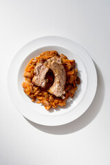 A hearty plate featuring a thick pork roast atop a warm bean and carrot stew. Rustic, comforting dish with rich savory flavors, perfect for dinner and family meals.