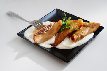 A plate of golden fried pastry rolls filled with meat rests on a creamy sauce. Garnished with fresh greens, the dish is presented on a sleek black plate for an elegant food photograph.