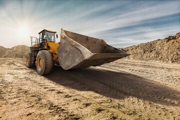 A large yellow bulldozer prepares to move earth at a construction site, illuminated by the warm...