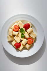 A white plate holds bite-sized gnocchi with a light cream sauce, accented by sliced strawberries and bright mint. Fresh, creamy, and inviting, this dessert showcases simple, fruity indulgence.