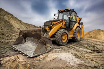 Obraz premium A heavy excavator loader moves dirt and rocks at a busy construction site, showcasing the power of modern engineering under a moody sky.