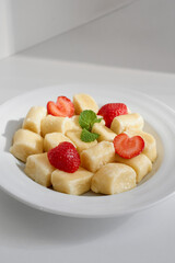 Creamy vareniki paired with bright strawberries, finished with a fresh mint garnish on a clean white plate for a simple, healthy dessert or snack. Perfect for bright, fruit-forward presentations.
