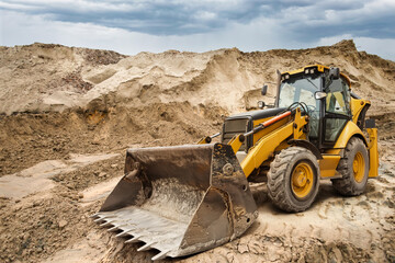 A yellow backhoe loader works on a construction site, moving dirt and debris while clouds gather ominously overhead, signaling possible rain